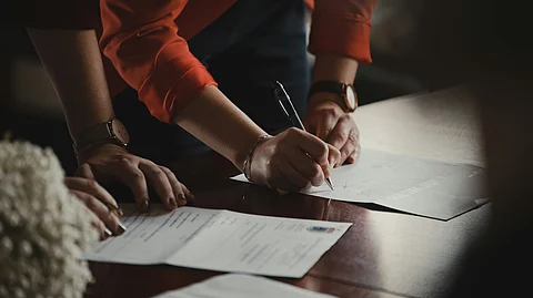 A pair of hands signing some paperwork and another set waiting to be signed.