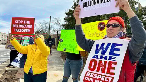 Group of protestors holding signs gathered outside. One of them read "stop the billionaire takeover".