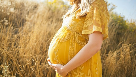 pregnant woman wearing yellow floral dress standing while touching her tummy