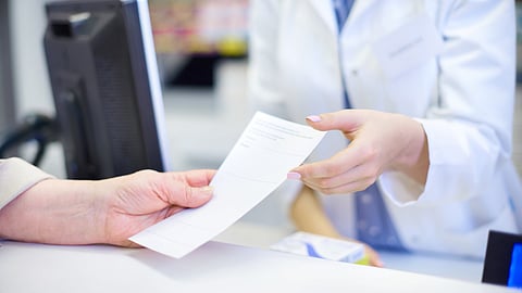 A person receiving a bill from another wearing a white coat indicating a healthcare setup.