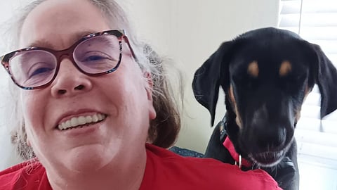 A picture of Tina posing with her service dog. She is wearing a red top in it.