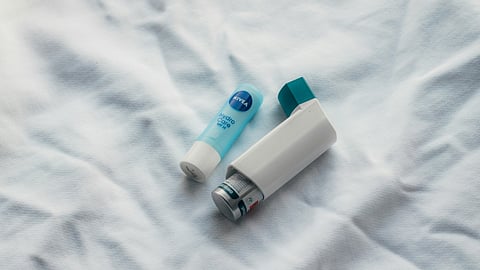 Close-up of asthma inhaler and nivea lip balm on a white cloth surface.