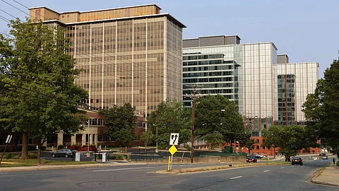 A street with two multi-rise buildings in a row. The street also shows an intersection with few vehicles on them.