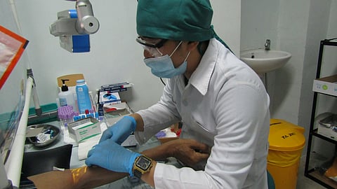 Person in white lab coat taking a blood sample from a person under sterile conditions.