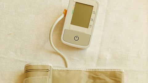Digital Blood Pressure Monitor and Pressure Cuff on White Fabric
