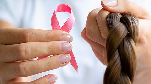 Close-up of a person holding up a pink ribbon bow in one hand and a braid of hair in another.