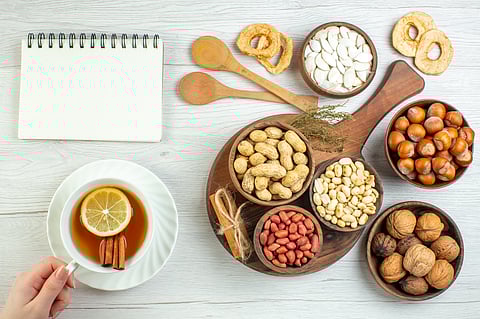 A variety of nuts displayed in wooden tableware. A person holding a tea with cinnamon and lemon in it.