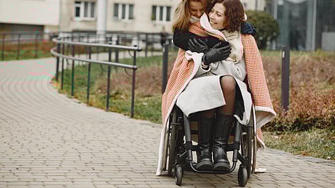 A woman in wheelchair is being hugged by another woman standing near her.