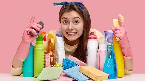 A woman wearing gloves with some household cleaners displayed in front of her.