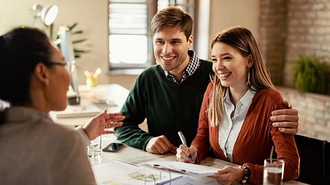 A couple is having a pleasant discussion with another female. They are about to sign some papers placed on the table.