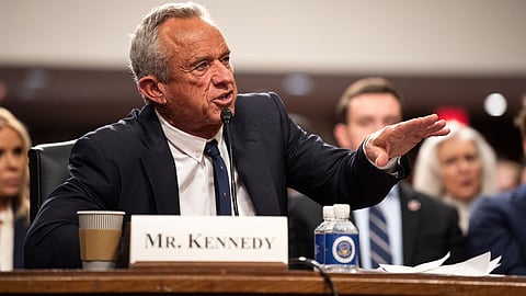 Robert F. Kennedy Jr. speaking at a podium with a nameplate that reads "Mr. KENNEDY".