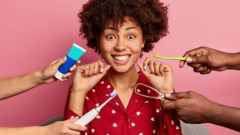 A girl holding floss and surrounded by toothbrushes and paste and other aids for oral care.
