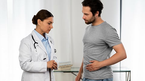 A male patient complaining of abdominal pain to a lady doctor dressed in a white coat.