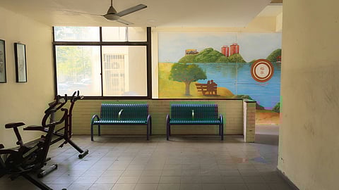 An indoor waiting room with some exercise equipment and two teal metal benches against the wall.