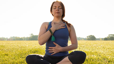 A woman is sitting outdoors in a meadow doing some meditation.