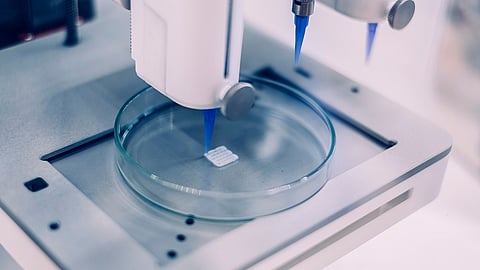 An image shows a printhead bioprinting a square-shaped construct in a petri dish.