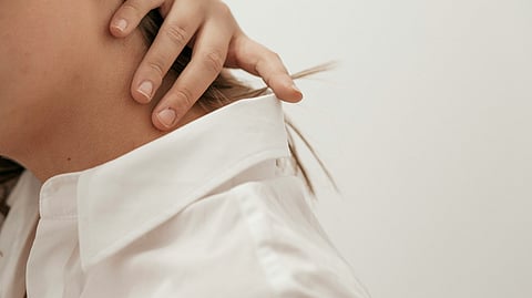 A woman clutching her back neck area indicating shoulder and neck pain.