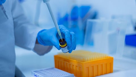 Scientist's gloved hand using a micropipette in a lab setting.