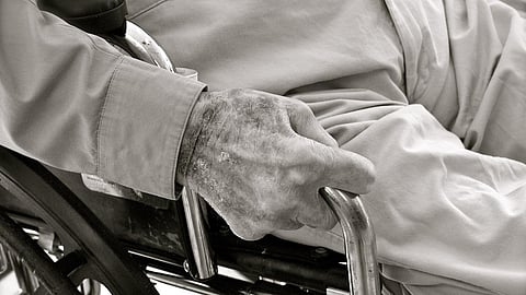 Elderly person's hand gripping wheelchair armrest in nursing home.