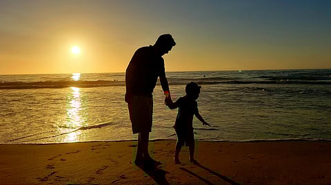 The tall person is enjoying the sunset view at the beach with his son. It displays happy emotions.