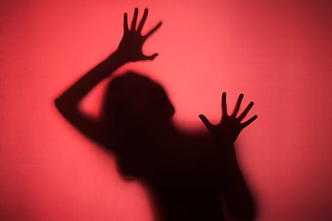 Silhouetted figure with hands pressed against a red background indicating assault.