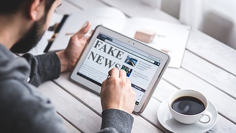 A person holds a tablet displaying FAKE NEWS on the screen.