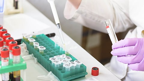 Laboratory setting with a scientist dropping liquids into many test tubes.