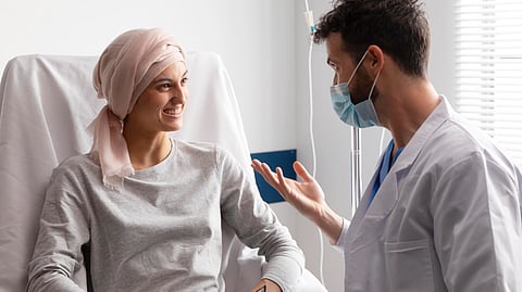 A female patient wearing a headscarf sitting on a hospital bed talking to masked male doctor.
