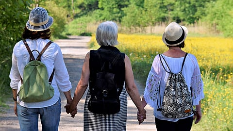 Three women walk hand in hand near a flower field.