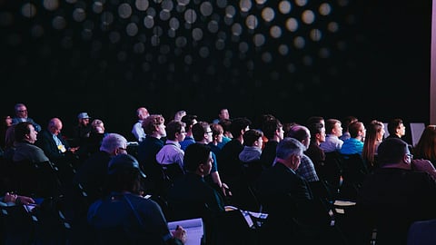 Many people sitting in a conference hall listening carefully and taking notes.