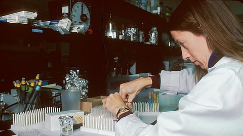A woman in a lab coat focused on her work at a laboratory bench, surrounded by scientific equipment.