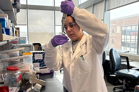 Adelaide Tovar wearing purple gloves is seen doing some experiment using a pipette in a laboratory.