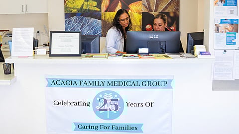 Sumana Reddy in white coat speaks to medical assistant Cynthia Ceja at the front desk.