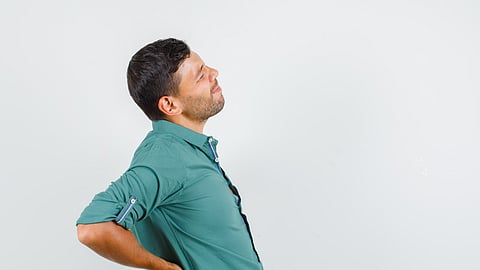 A person experiencing lower back pain, clutching their back with visible signs of discomfort.