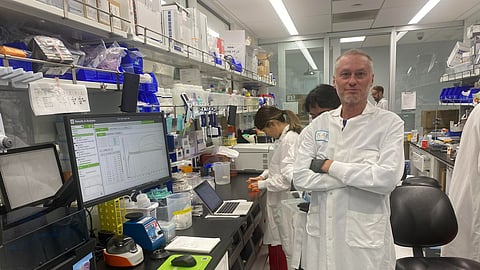 Tim Friede in a lab coat at a lab with his colleagues working in the back.