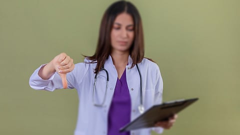 Displeased young woman doctor wearing white coat, showing thumbs down