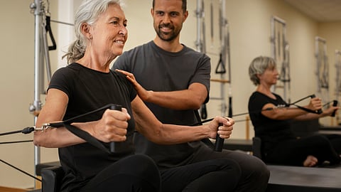 An elderly woman in black outfit is being instructed by a coach how to do certain exercises.