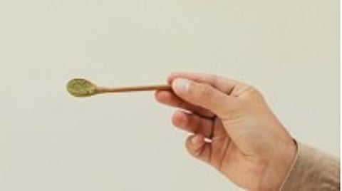 A person is displaying a spoon with green powder, probably kratom.