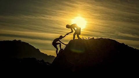 Picture shows one person helping the other climb up a foothill.