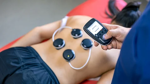 A woman using nerve stimulating devoice on her back with a remote.