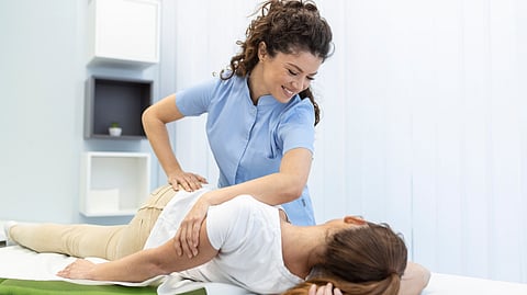 A young woman chiropractor is helping a lady in doing some alignment moves on a table.