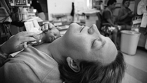 A black and white image where a mother has kept a low birth preterm baby on her bare chest inside an ICU.