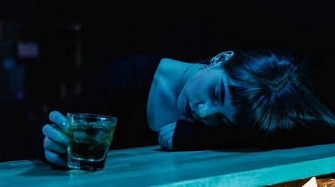 A woman resting her head on a counter with a glass of alcohol in her hand.