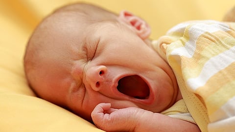 An Infant wrapped in a yellow attire yawning in his sleep.