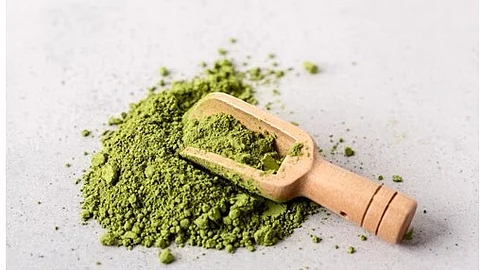 A green powder being scooped in a wooden spoon.