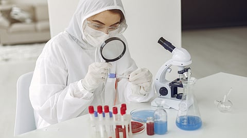 Scientist in full protective gear examining a sample through a magnifying glass.