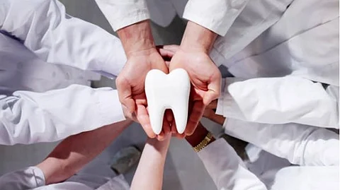 Multiple people wearing white coat placing their hands together to hold a tooth model.