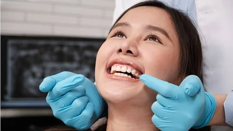 A young lady at a dentist office and a doctor wearing blue gloves examining her teeth.