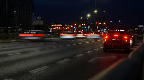 A night photo of a road with moving cars, creating light trails.