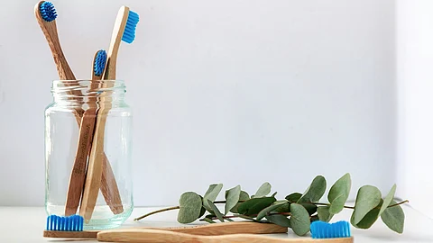 A glass jar holding bamboo toothbrushes with blue bristles